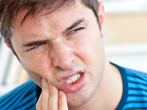 man holding side of mouth in pain