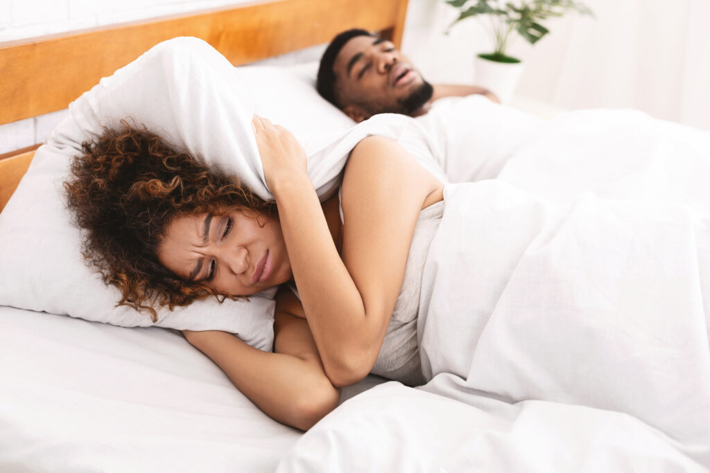 Tired Woman Covering Her Ears While Husband Snores