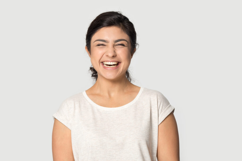 young woman in casual weat t-shirt posing isolated on grey studio background laughing