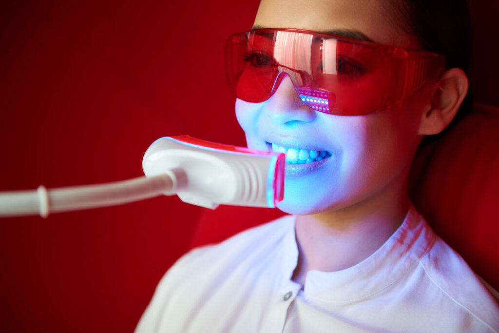Close up portrait of happy asian woman wearing red protection glasses to have tooth whitening procedure in beauty center