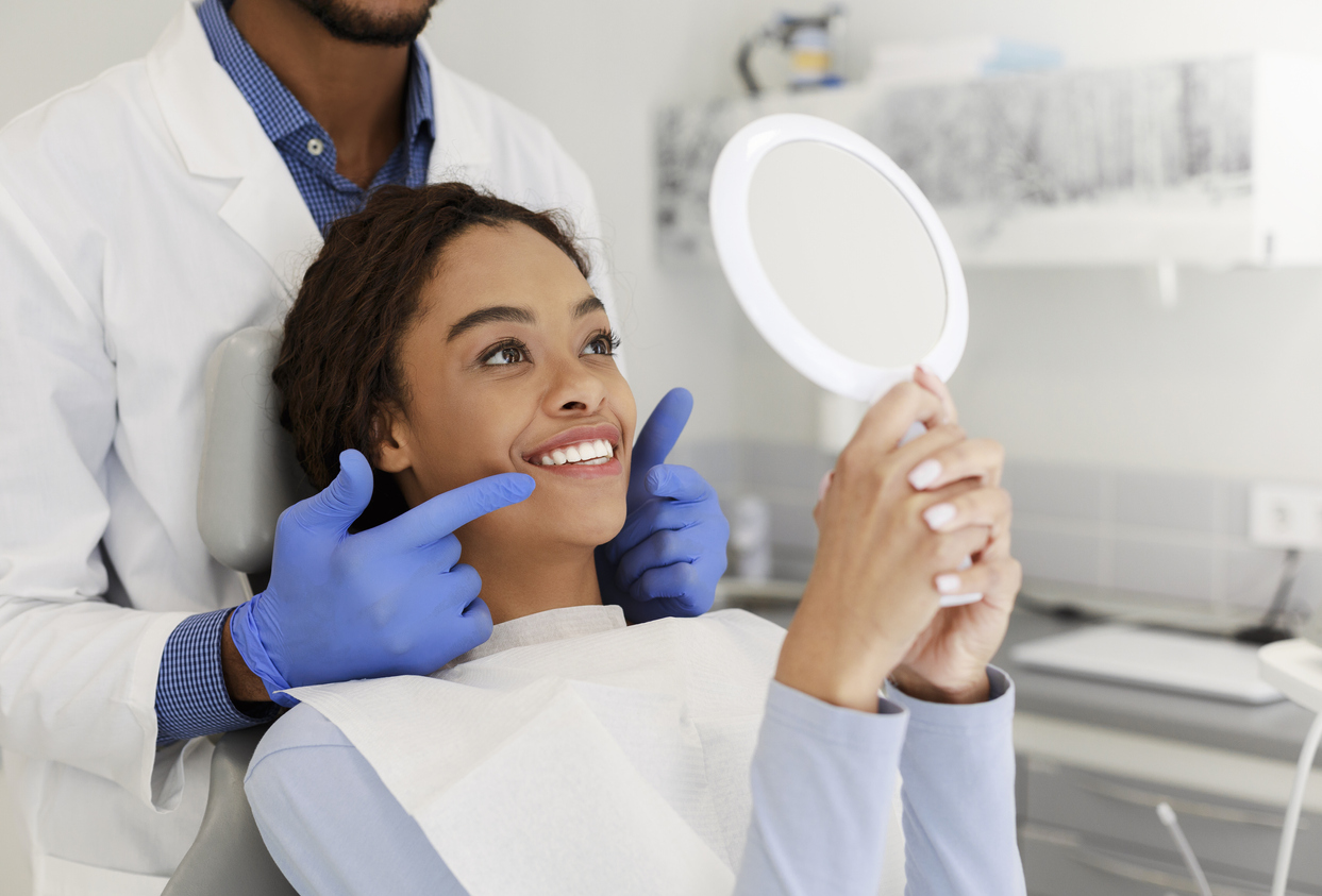 A dentist and patient look in a mirror at the patient's freshly whitened teeth.