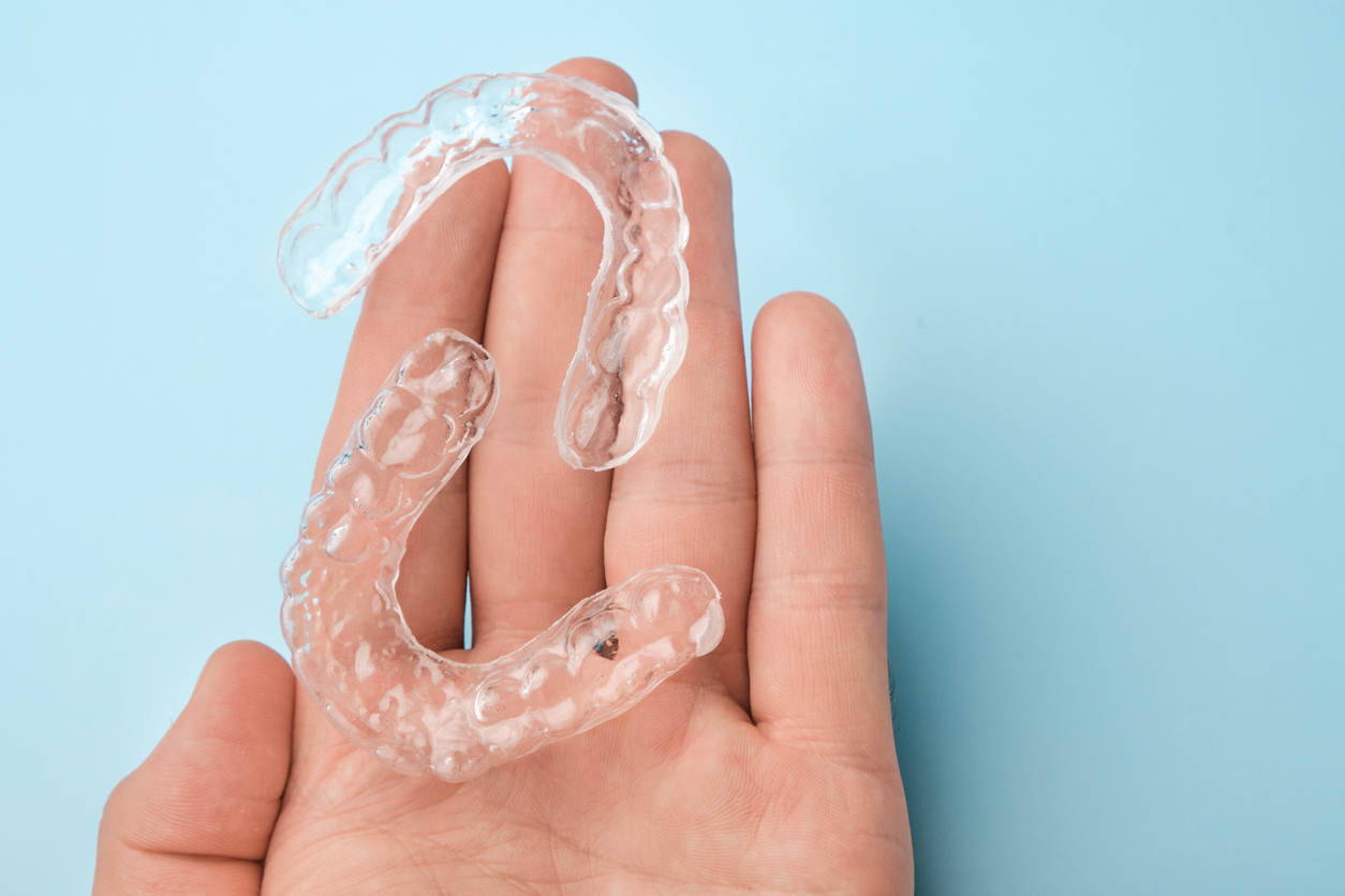 A person holds a set of Invisalign clear aligners in their hand.