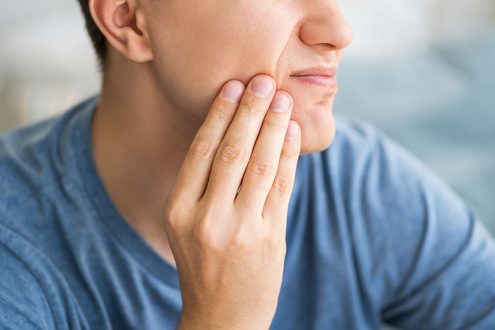 A person holds their jaw because of TMJ pain.