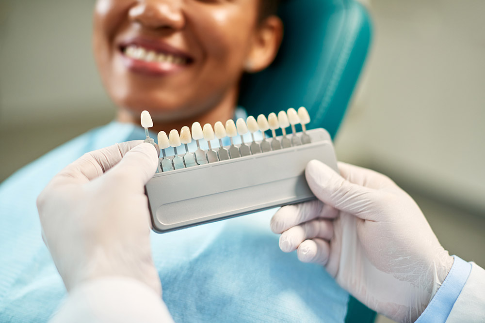 A dentist shows a patient a selection of dental veneers on a rack.